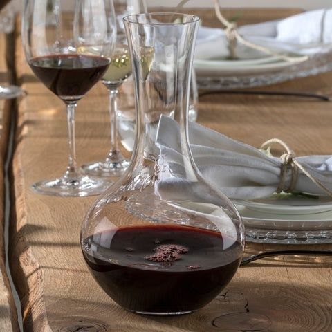 Red wine in a decanter and glass beside a set dining table