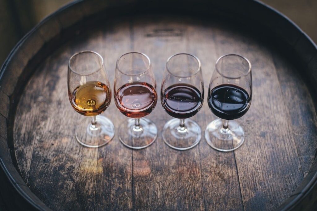 Four wine glasses holding wines of different colors on a wooden barrel